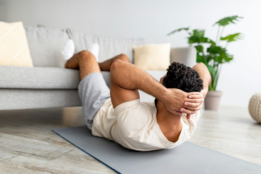 Fit young Arab guy exercising abs muscles on yoga mat at home. Domestic fitness concept