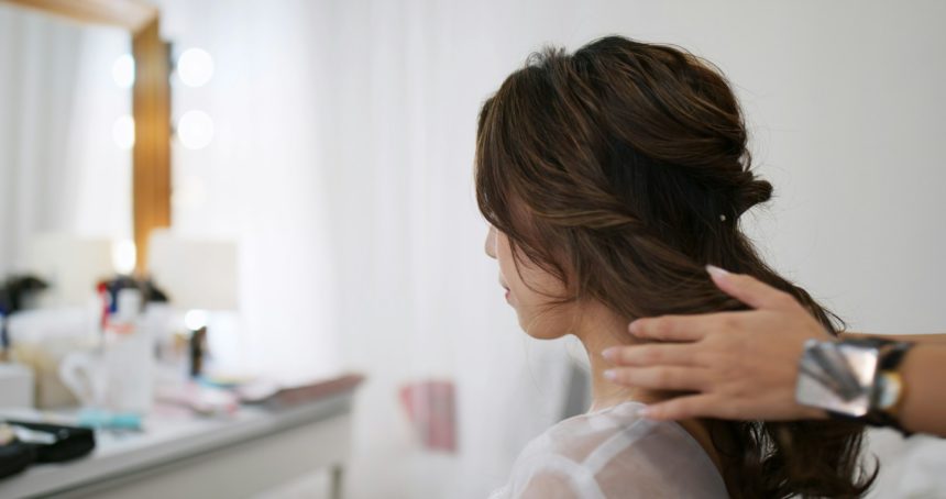 Hairdresser making hairstyle on bride in beauty salon