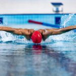 Professional male swimmer in swimming cap and goggles in motion and action during training at pool